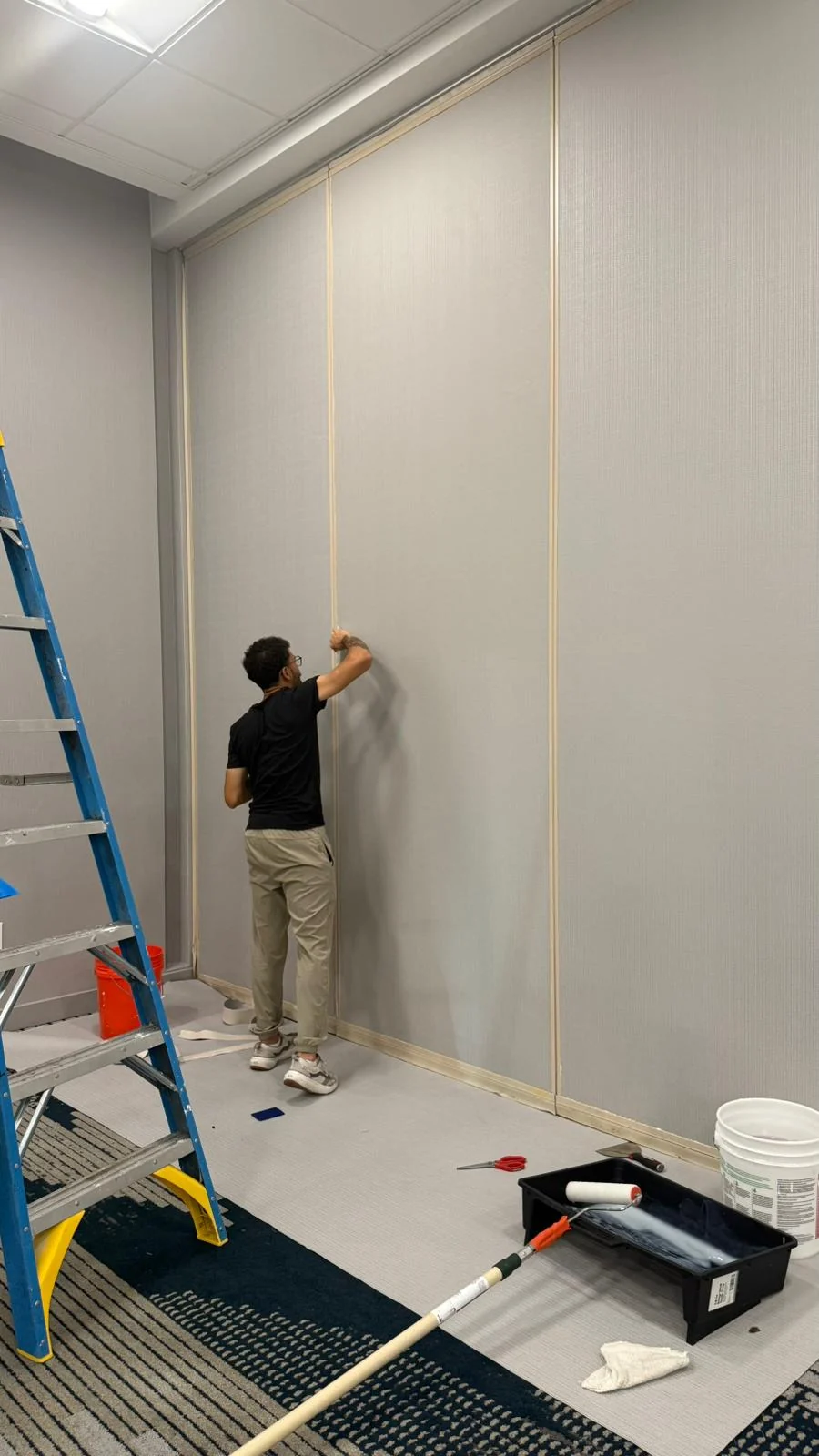 Installer smoothing wallcovering between protected vertical trim with tools nearby · Hotel Alba Tampa, Tapestry Collection by Hilton