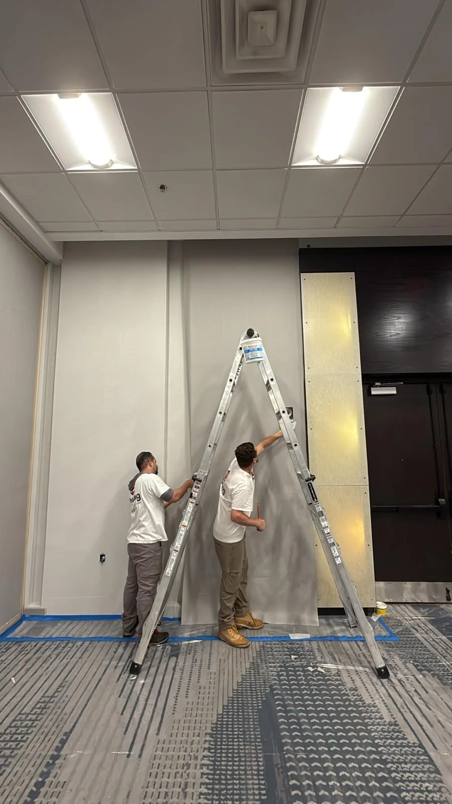 Crew positioning a length of wallcovering beside the ballroom doorway · Hotel Alba Tampa, Tapestry Collection by Hilton
