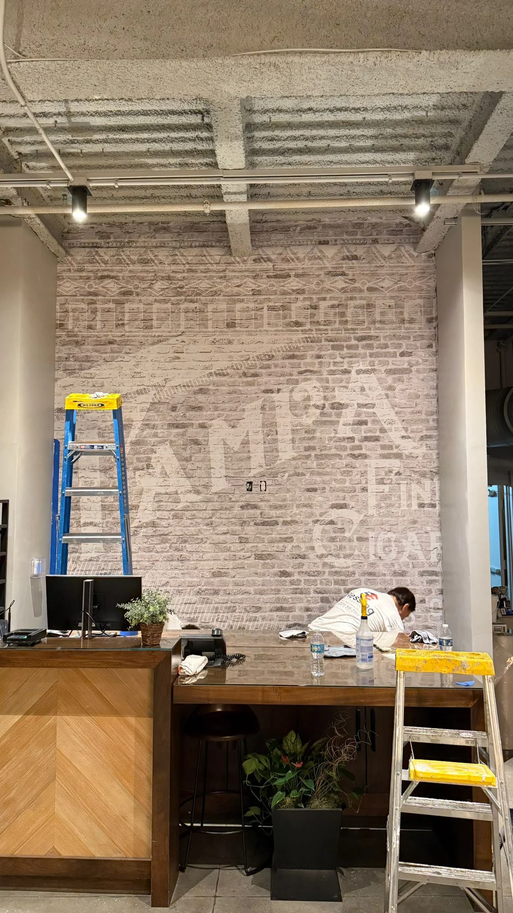 Brick-pattern wallcovering in place across the lobby feature wall with ladders and tools still present · Hotel Alba Tampa, Tapestry Collection by Hilton