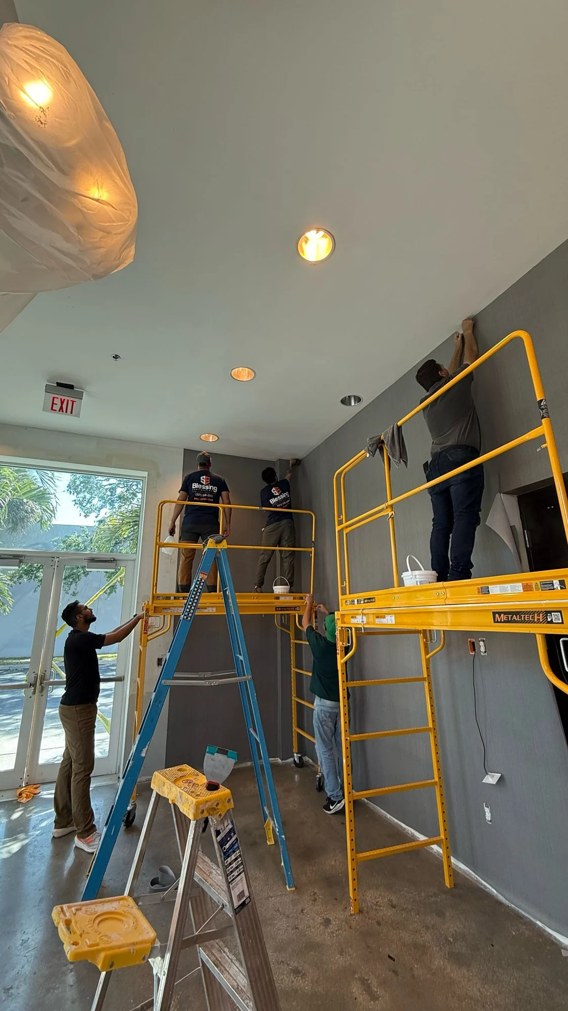 Crew installing wallcovering at the ceiling line near the entrance · Hotel Alba Tampa, Tapestry Collection by Hilton