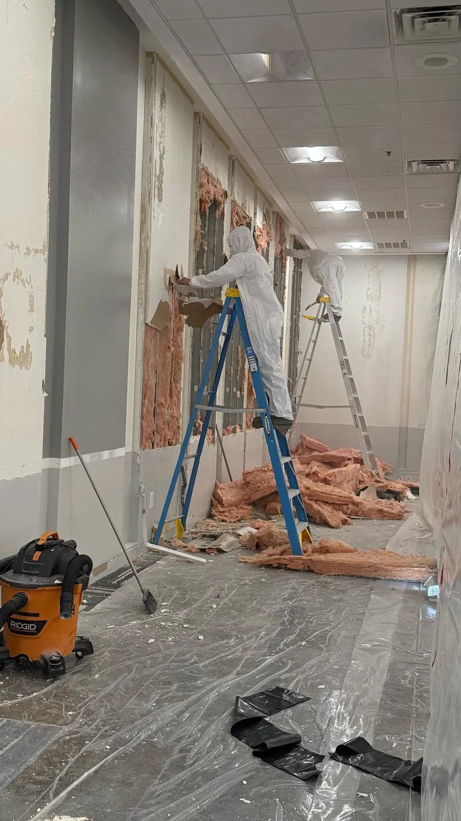 Crew removing wall material from ladders with protective floor sheeting in place · Tapestry Collection by Hilton