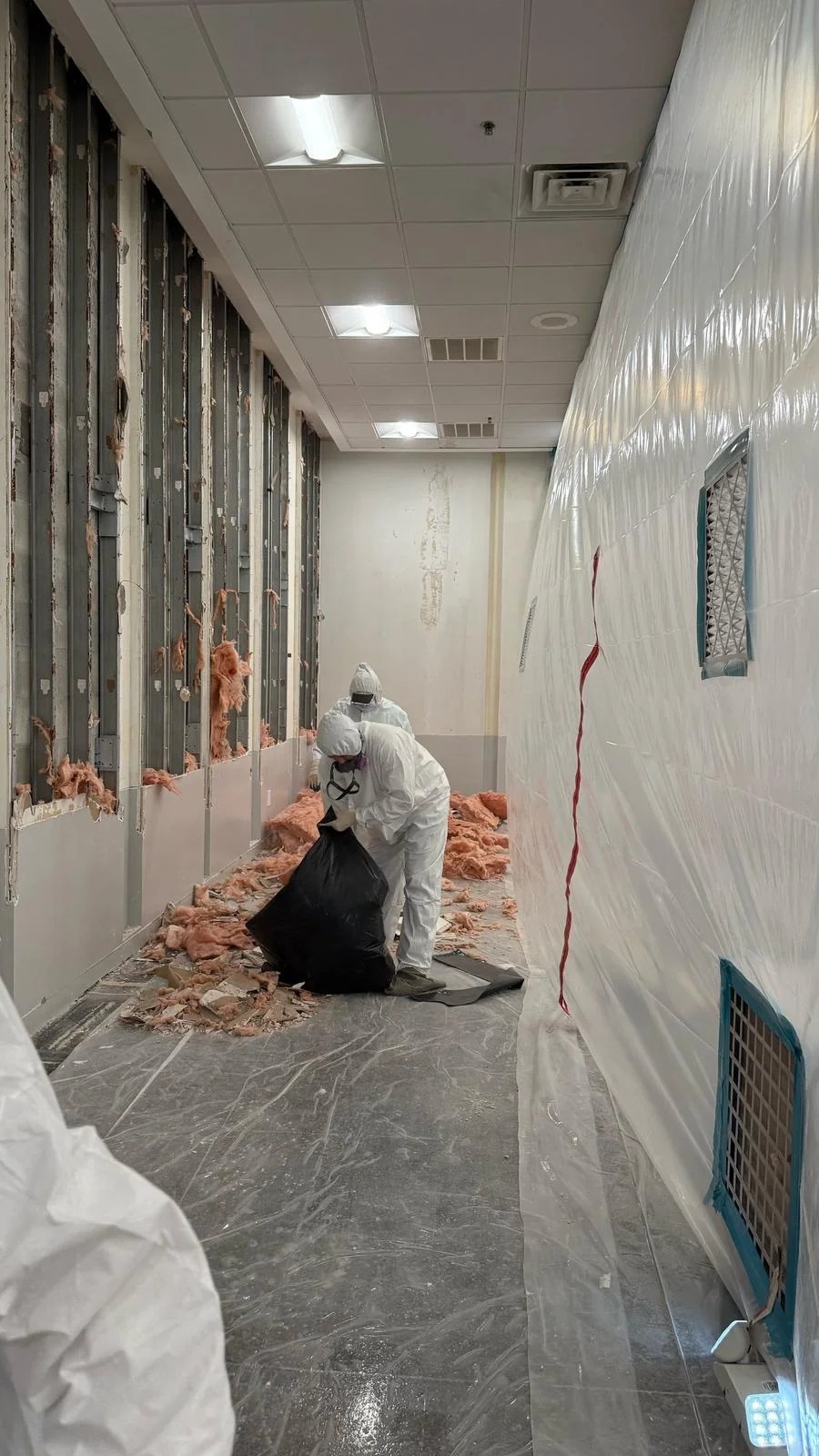 Crew collecting removed wall material inside the plastic-sheeted work area · Tapestry Collection by Hilton