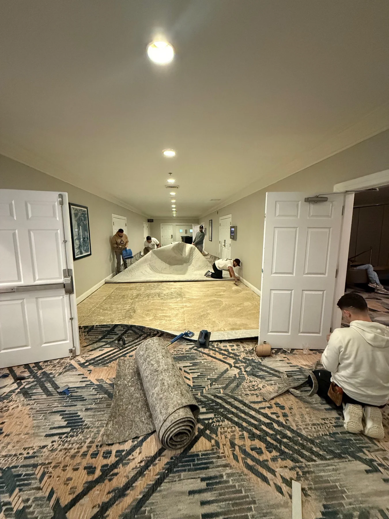 Crew laying carpet along the meeting-room corridor with an exposed floor section and carpet roll nearby at DoubleTree by Hilton, Jacksonville