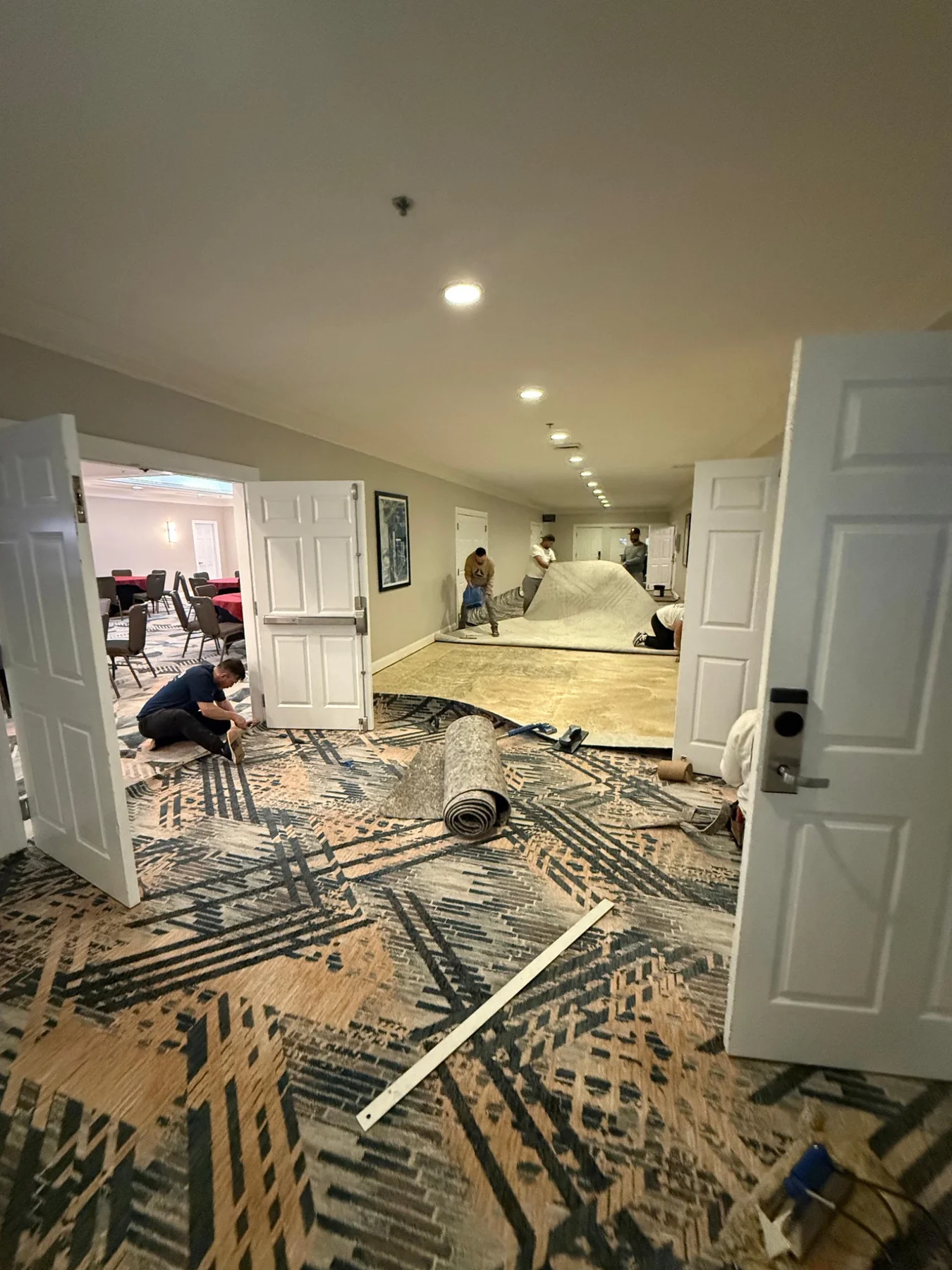 Crew fitting patterned carpet beside the open meeting-room doors with tools and a carpet roll nearby at DoubleTree by Hilton, Jacksonville