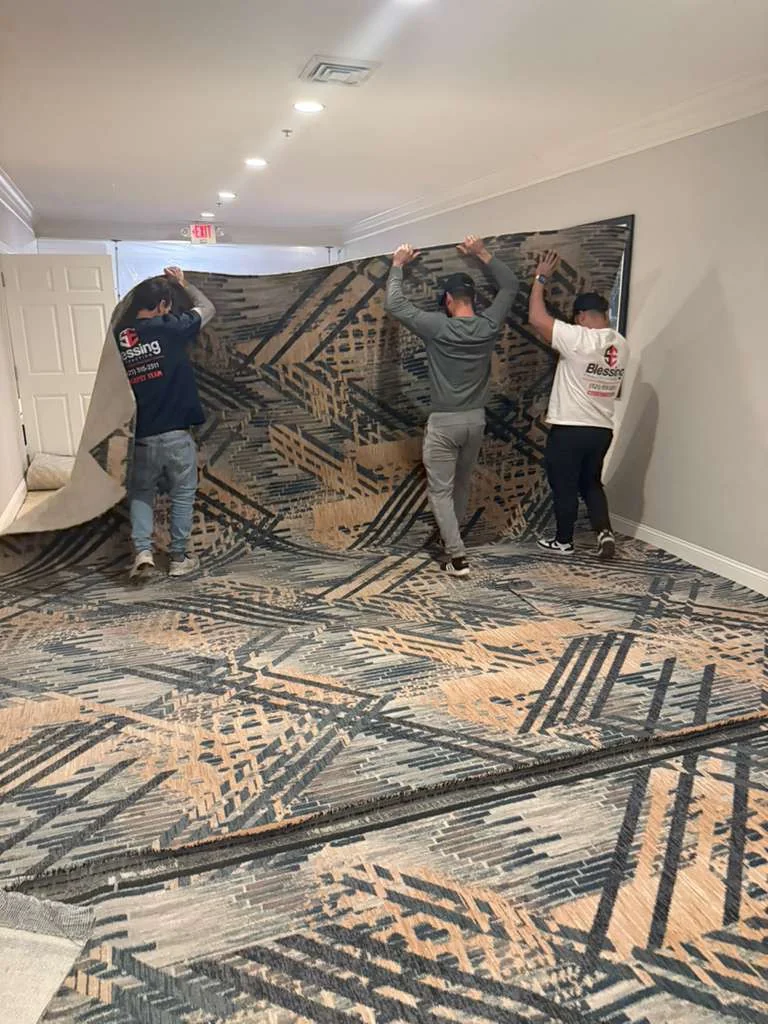 Three crew members lifting and positioning a length of patterned carpet in the corridor at DoubleTree by Hilton, Jacksonville