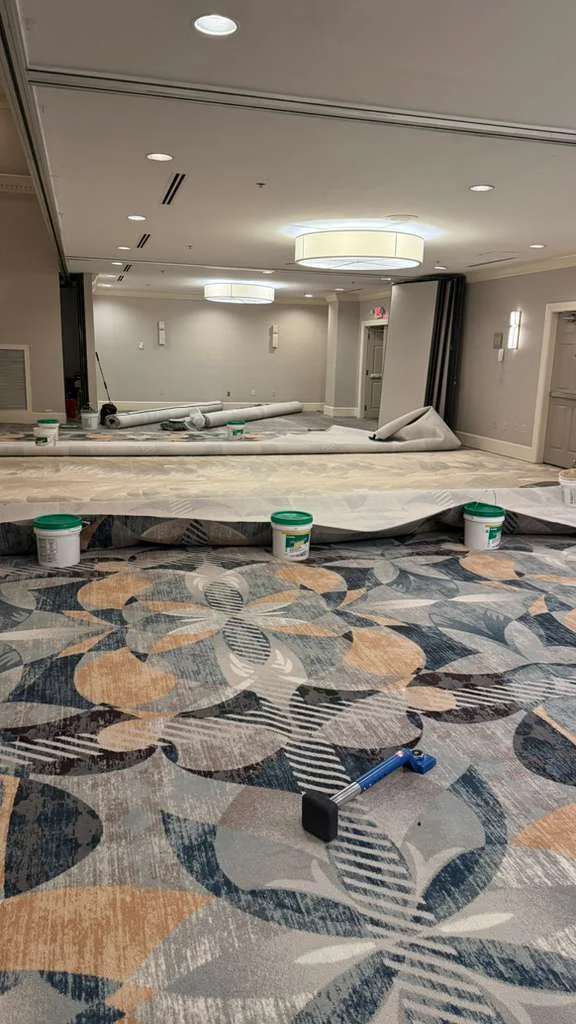 Patterned carpet installation in progress, with carpet rolls and tools in a DoubleTree by Hilton ballroom section