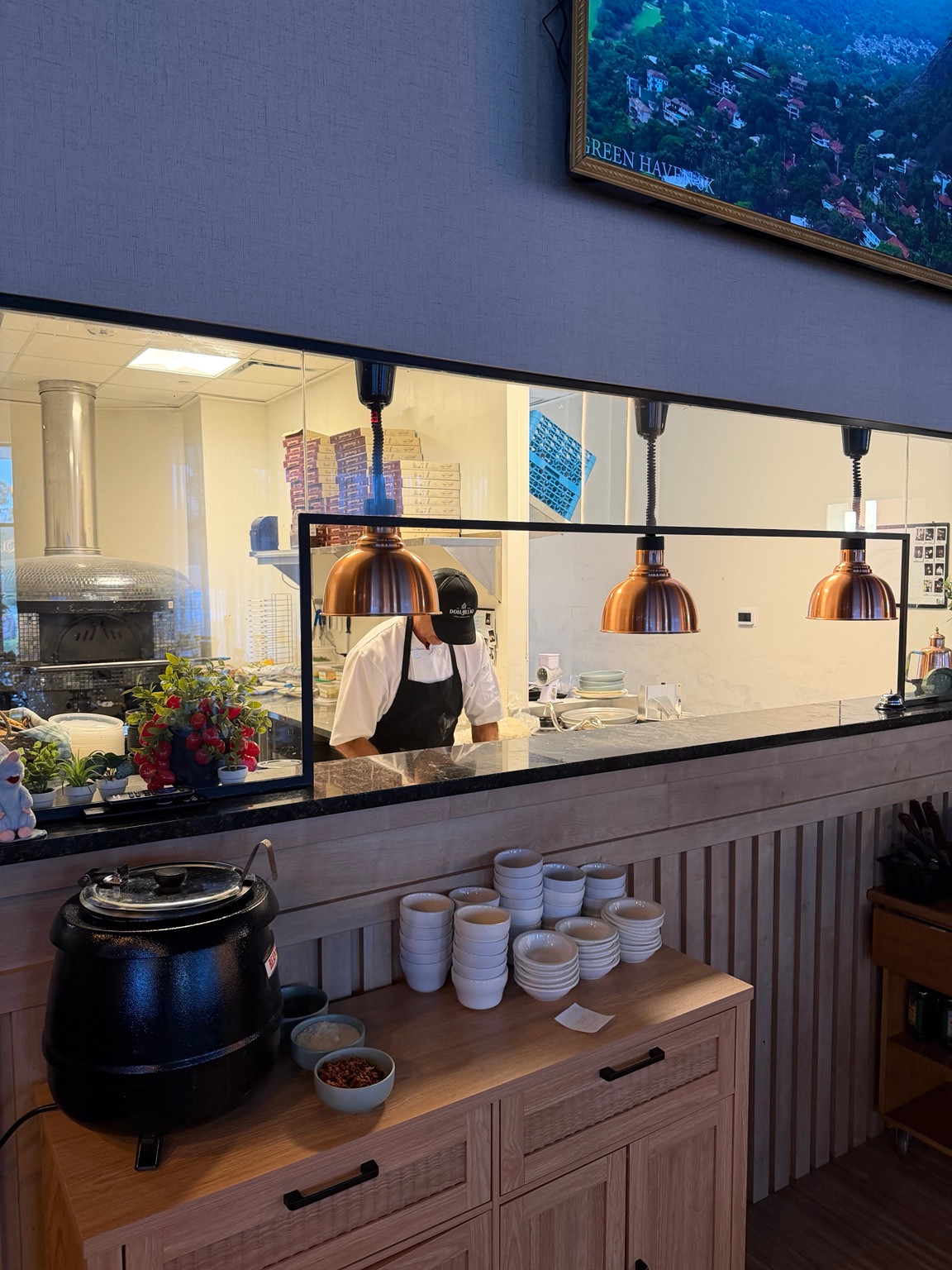 Finished kitchen service opening with counter, cabinetry and three copper-colored pendant lamps
